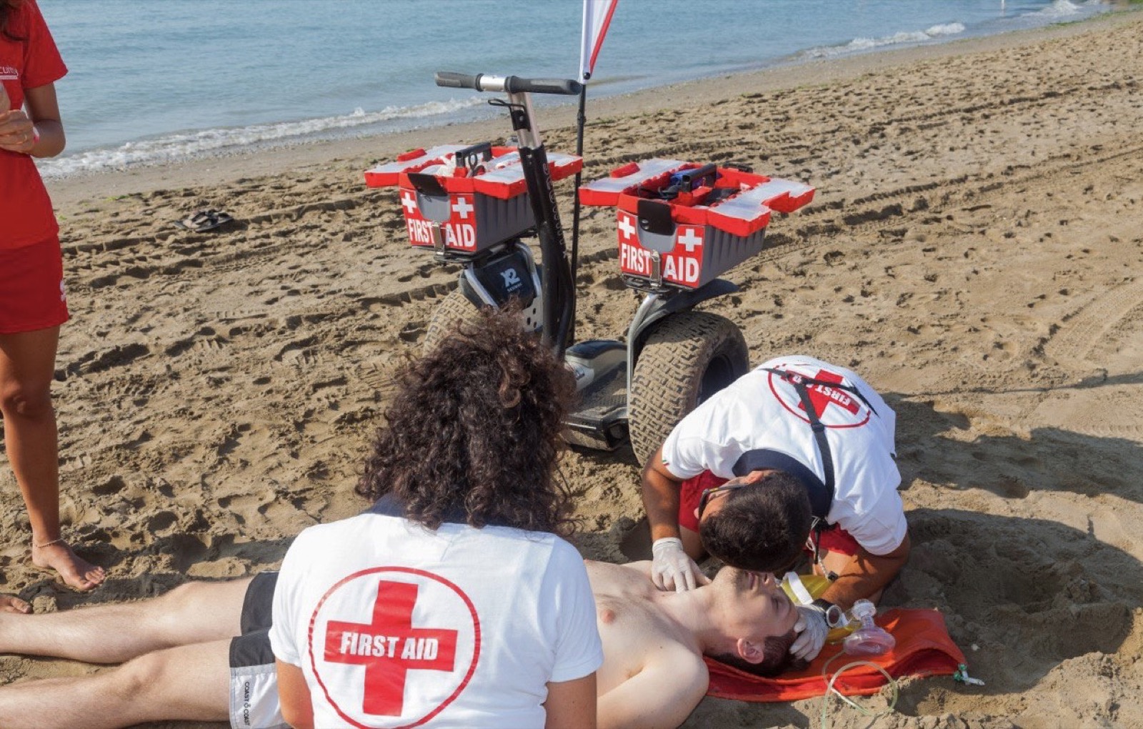 Soccorritori First Aid prestano primo soccorso a un bagnante in spiaggia, con il Segway attrezzato