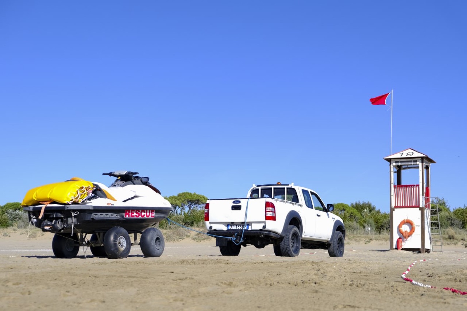 Pickup con carrello e moto d'acqua di soccorso in spiaggia accanto alla torretta
